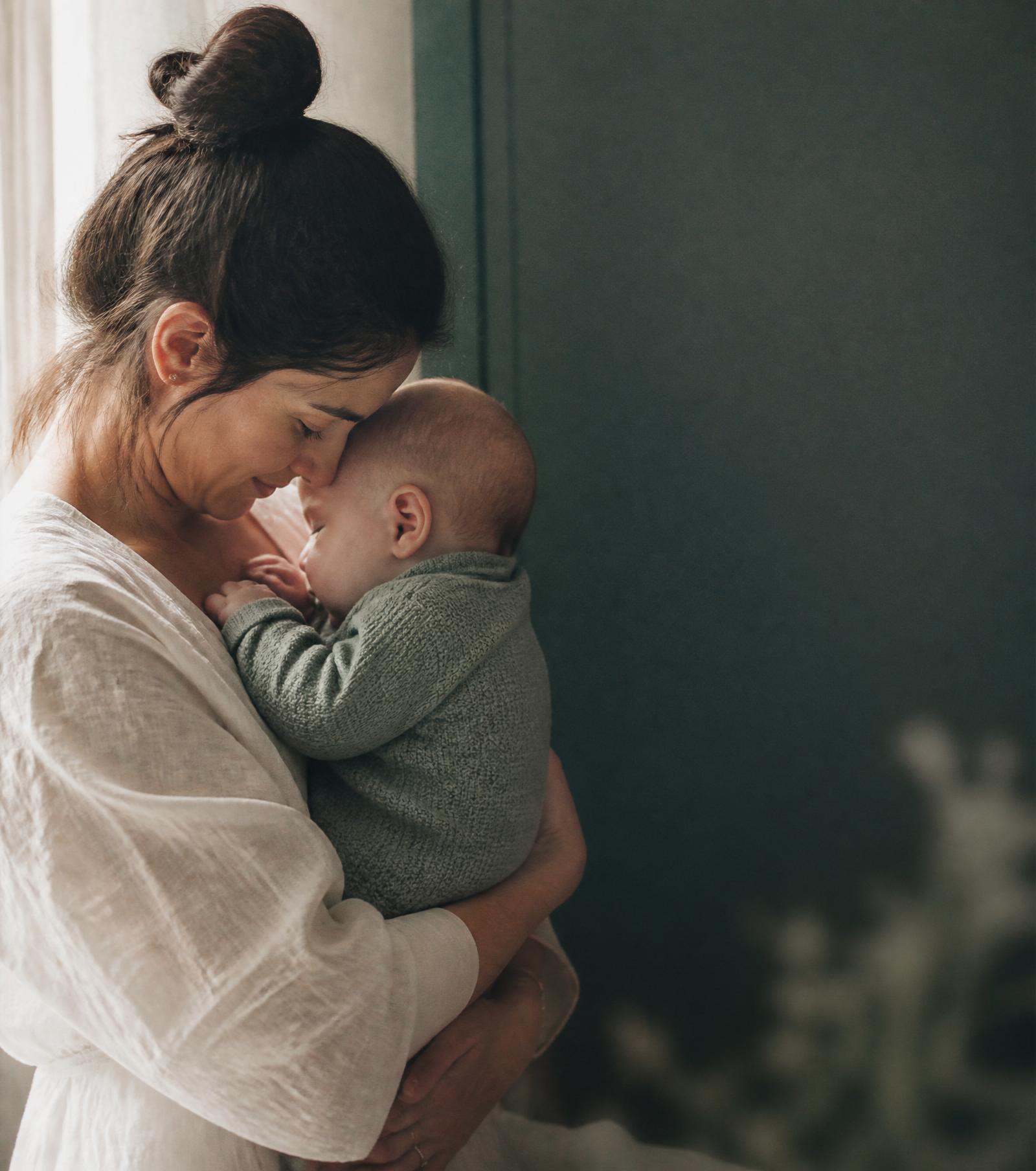 A mother holding her infant close in soft window light